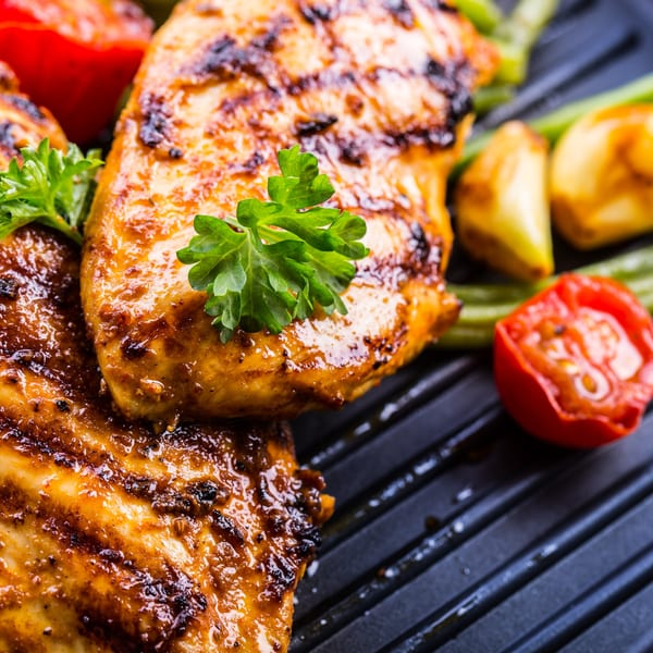 Grilled CFC chicken breasts with parsley, roasted tomatoes, and green beans on a dark griddle.