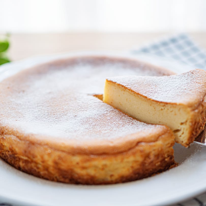A whole cheesecake dusted with powdered sugar, with one slice being lifted out.