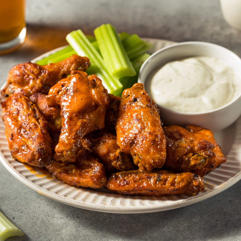 A plate of CFC Fried Chicken buffalo wings with celery sticks and a side of ranch dressing.